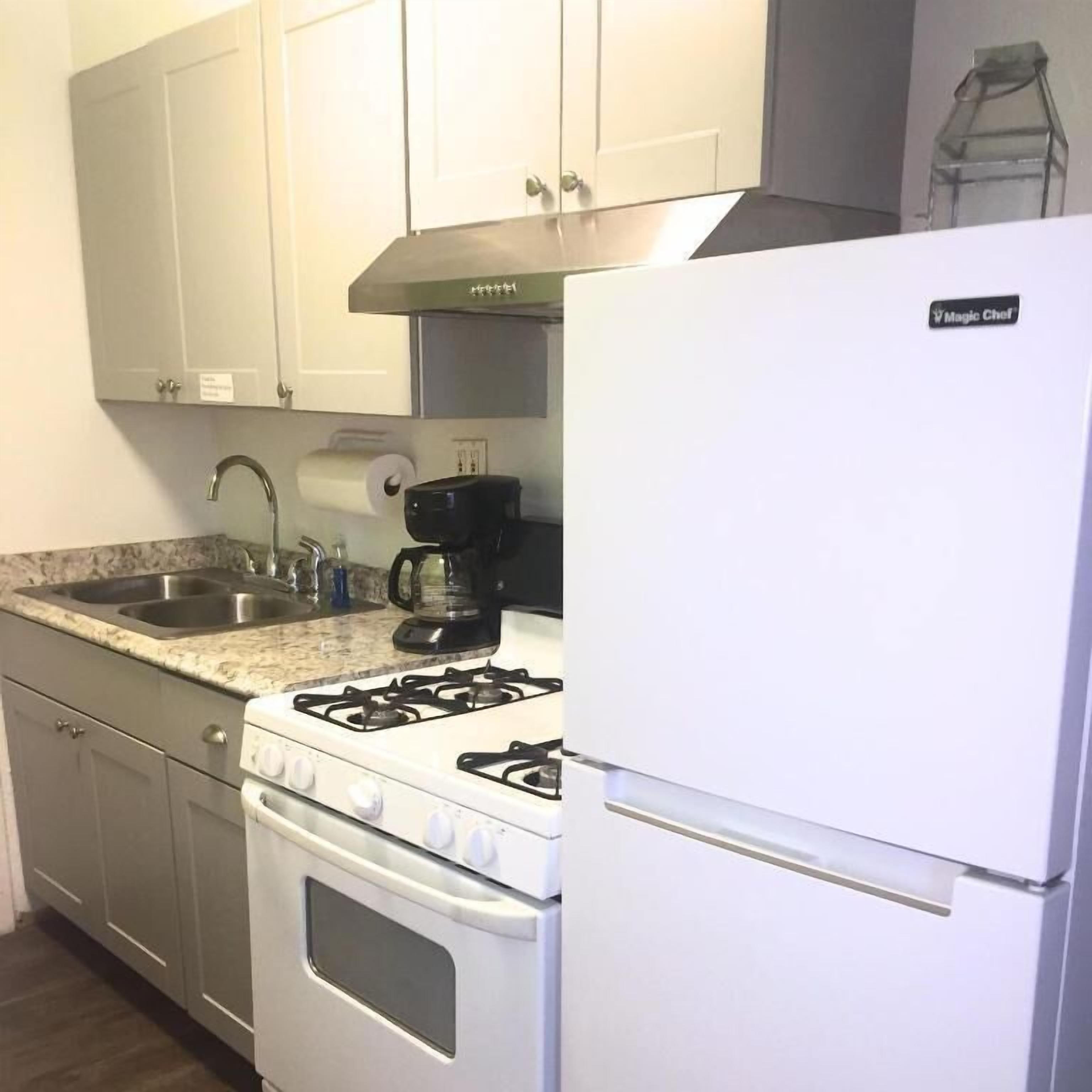 A kitchen with a gas stove, a coffee maker, a refrigerator, and a sink.