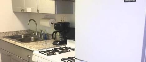 A kitchen with a gas stove, a coffee maker, a refrigerator, and a sink.