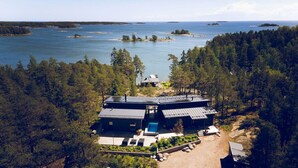 Ett modernt hus med en stor terrass, omgivet av tät skog och en sjö eller ett annat vattendrag.