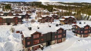Een besneeuwde vakantiebestemming met meerdere chalets, een piste in de verte en een heldere lucht.