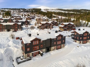 A snow-covered resort with multiple chalet-style buildings, a ski slope in the background, and a clear sky. - Ski-in/Ski-out apartment with Sauna in Trysil REF:TH720 (Trysil)