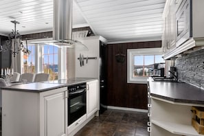 A modern kitchen with white cabinetry, a built-in oven, a large island with a sink, and a view through a window. - Ski-in/Ski-out apartment with Sauna in Trysil REF:TH720 (Trysil)