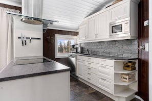 A modern kitchen with white cabinetry, a built-in microwave, and a stone backsplash. - Ski-in/Ski-out apartment with Sauna in Trysil REF:TH720 (Trysil)