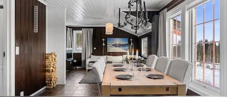 A modern dining area with a wooden table, white chairs, and a chandelier.