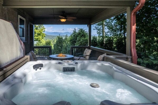 A hot tub with a fire feature, surrounded by outdoor furniture, set on a porch with a mountain view. - Experience comfort in Bryson City at Smoky Ridge (Bryson City)