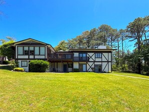 A two-story house with a balcony, surrounded by a well-maintained lawn and trees.