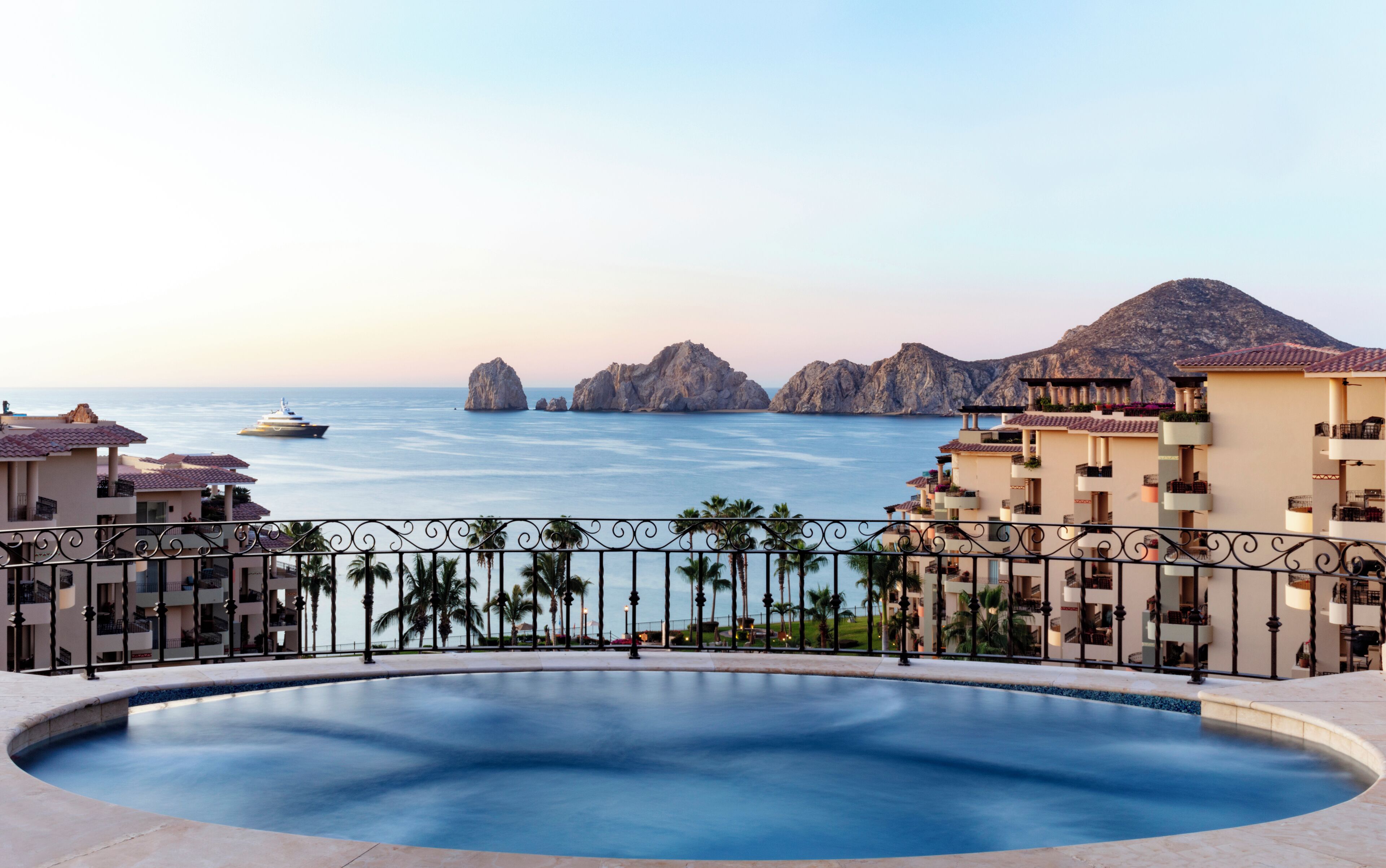 A resort pool with a view of the sea and rocky formations.