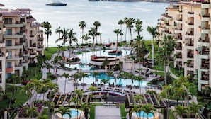 Un resort con varias piscinas, palmeras y vistas al mar y a las montañas.