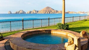 Un jacuzzi con borde de piedra, cerca metálica y vistas al mar y a las montañas.
