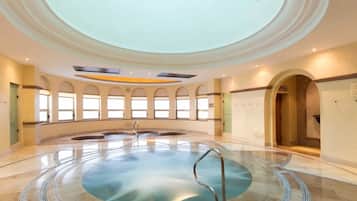A large indoor swimming pool with a circular design, surrounded by arched windows and a high ceiling.