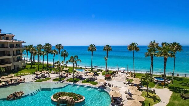 Un resort con una piscina grande, palmeras y vista al océano.
