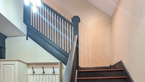 Un escalier avec des marches en bois et une main courante sombre, menant à un palier sur lequel est fixé un luminaire.