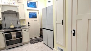 Une cuisine équipée d’une cuisinière, d’un four et de placards. Elle comporte deux fenêtres et une porte.