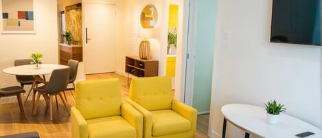 A modern living room with a yellow sofa set, a dining area with a round table and chairs, and a small white table with a plant.