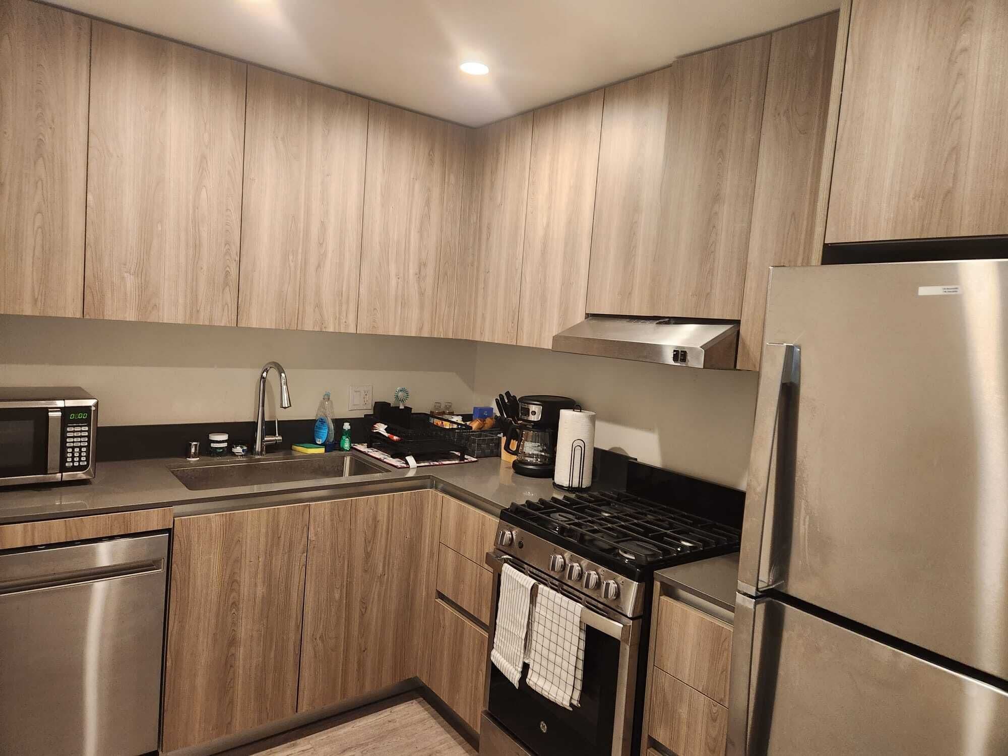 A modern kitchen with wooden cabinets, stainless steel appliances including a microwave, sink, stove, and refrigerator.