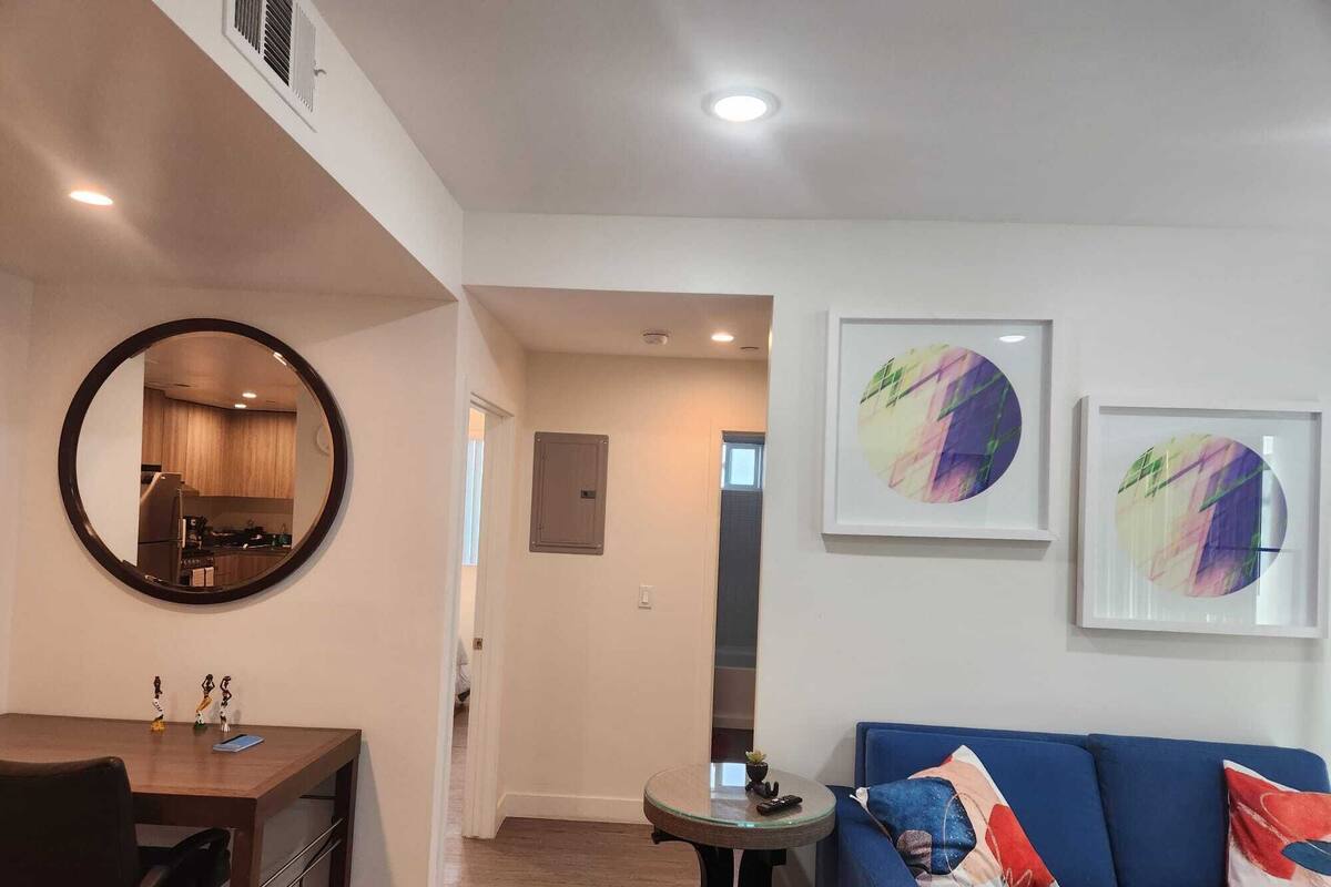 Una sala de estar moderna con un espejo redondo, un sofá azul con cojines coloridos y dos cuadros abstractos en la pared.