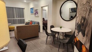 Un salon moderne avec un canapé, une table à manger et des chaises, un miroir rond et des œuvres d’art accrochées aux murs.