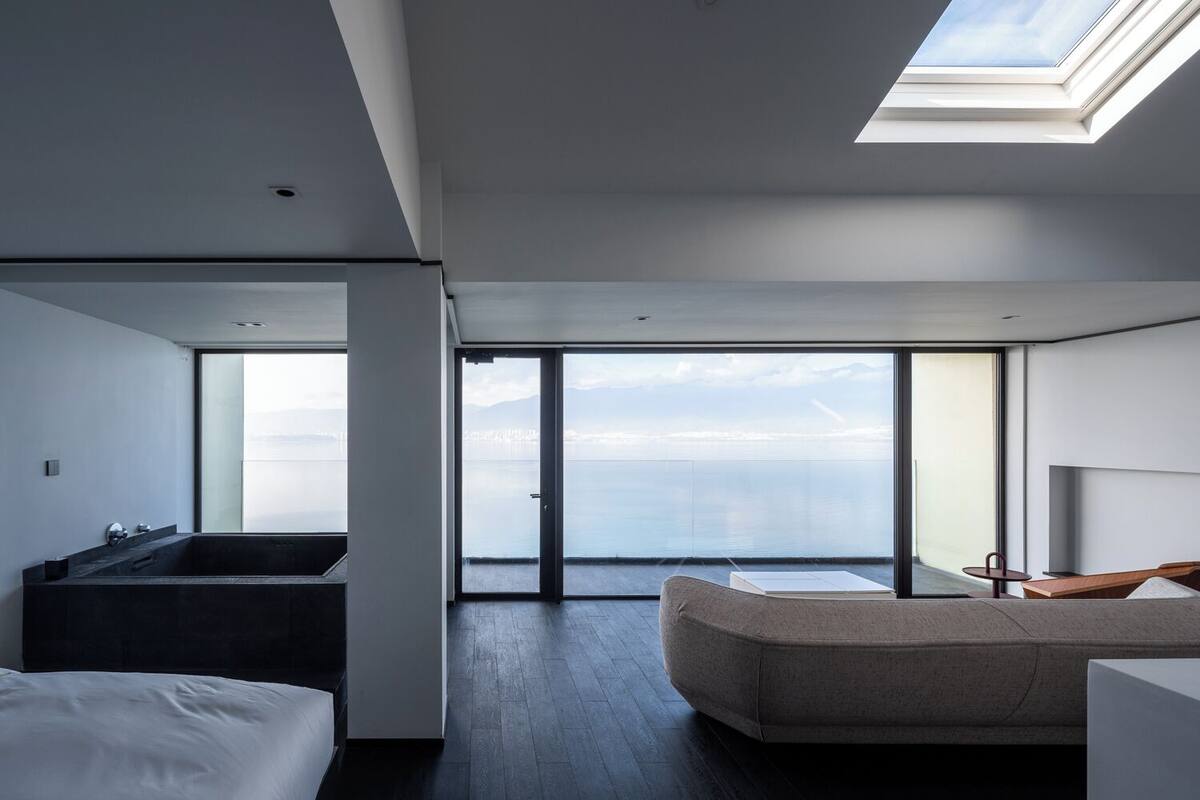 Ein modernes Hotelzimmer mit einem großen Oberlicht, einer Badewanne, einem Sofa und Blick auf das Meer.