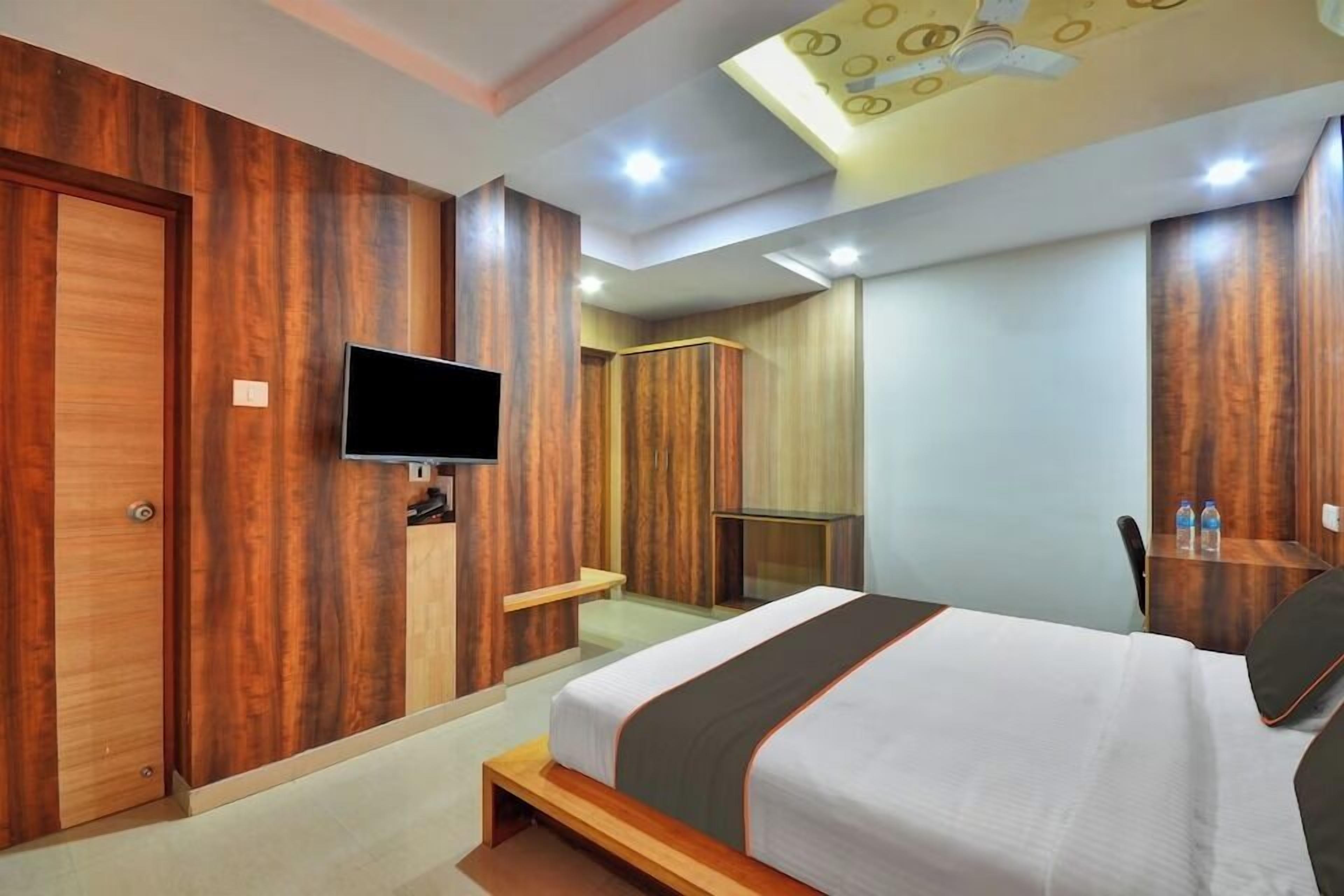 Una habitación de hotel moderna con una cama grande, paneles de madera, televisión y una lámpara en el techo.