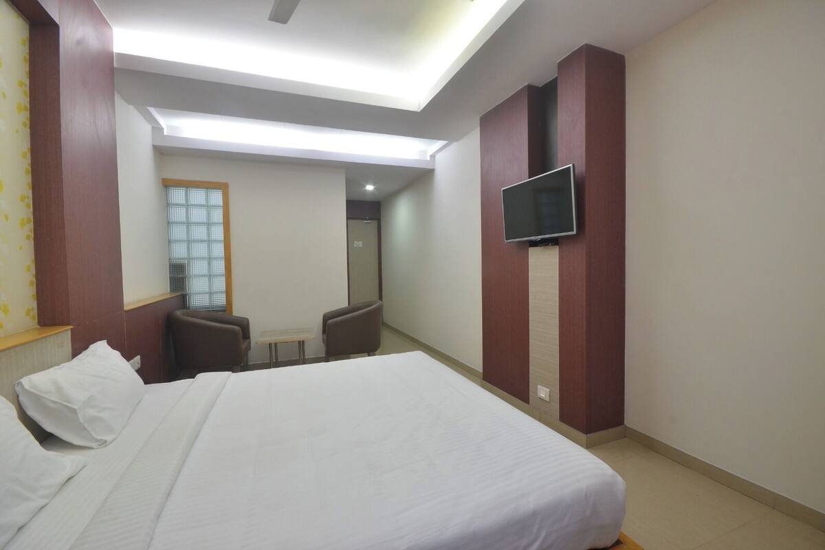 A hotel room with a large bed, a TV mounted on the wall, a small table, and two chairs.