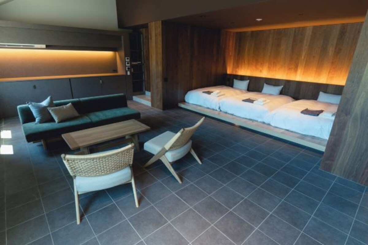 Una habitación de hotel moderna con una cama grande, un sofá, una mesa de comedor y sillas de mimbre.