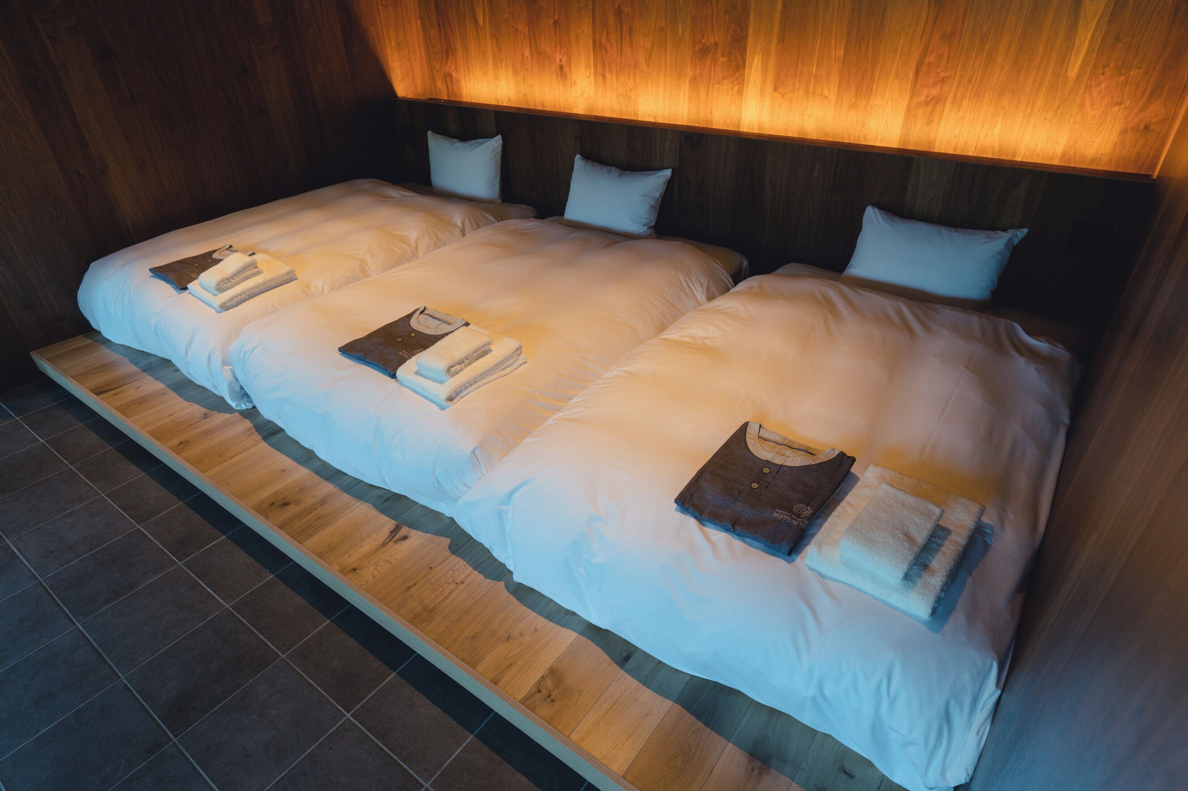 A room with a wooden floor, a large bed with white bedding, and a wooden headboard.