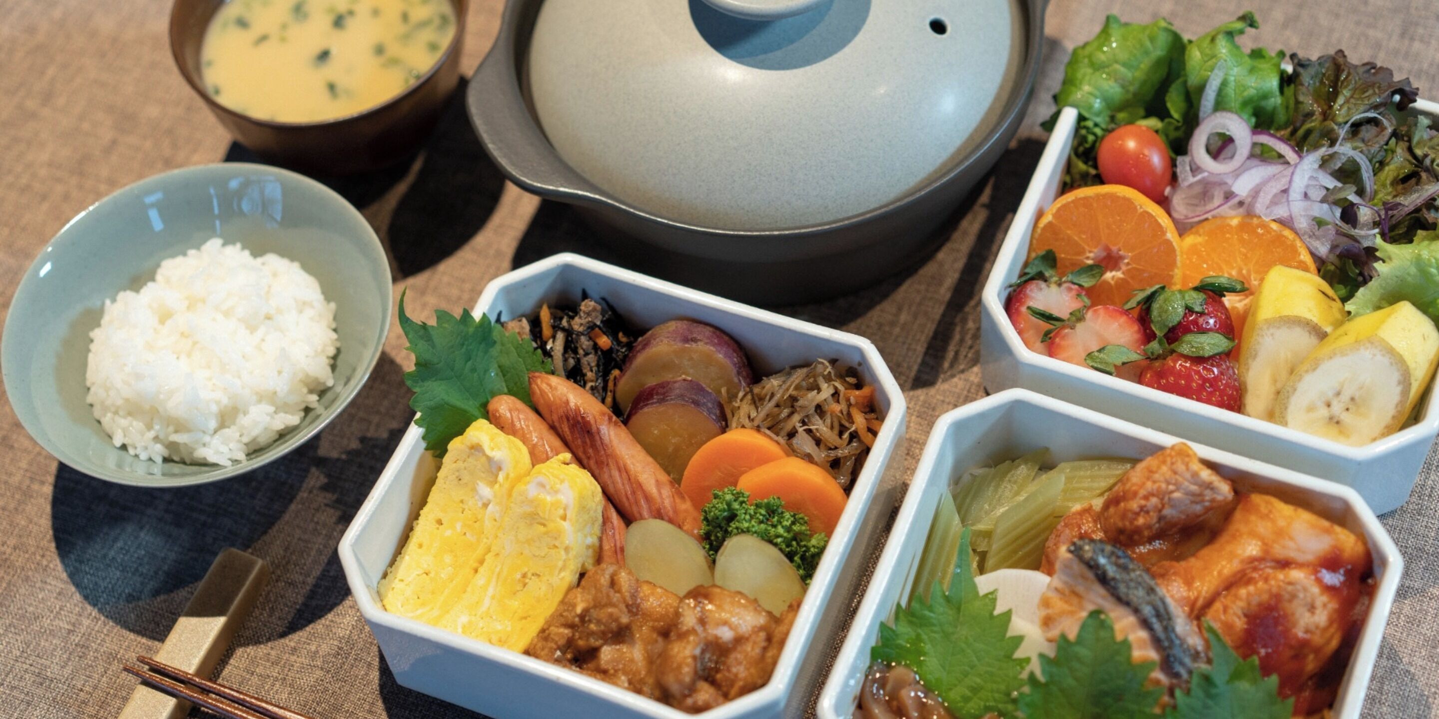 A variety of dishes including rice, eggs, vegetables, and meat, arranged on a table with chopsticks and bowls.