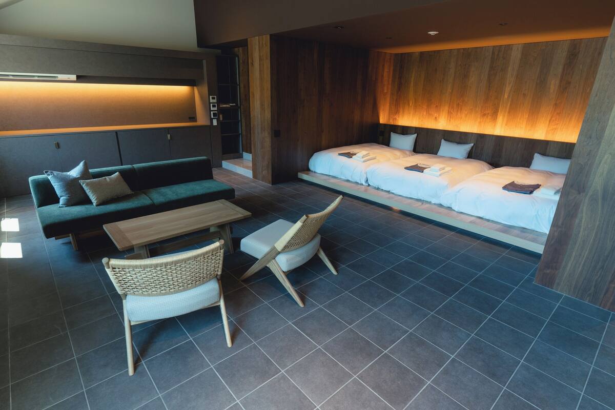 A modern hotel room with a sofa, a dining table, and two beds.