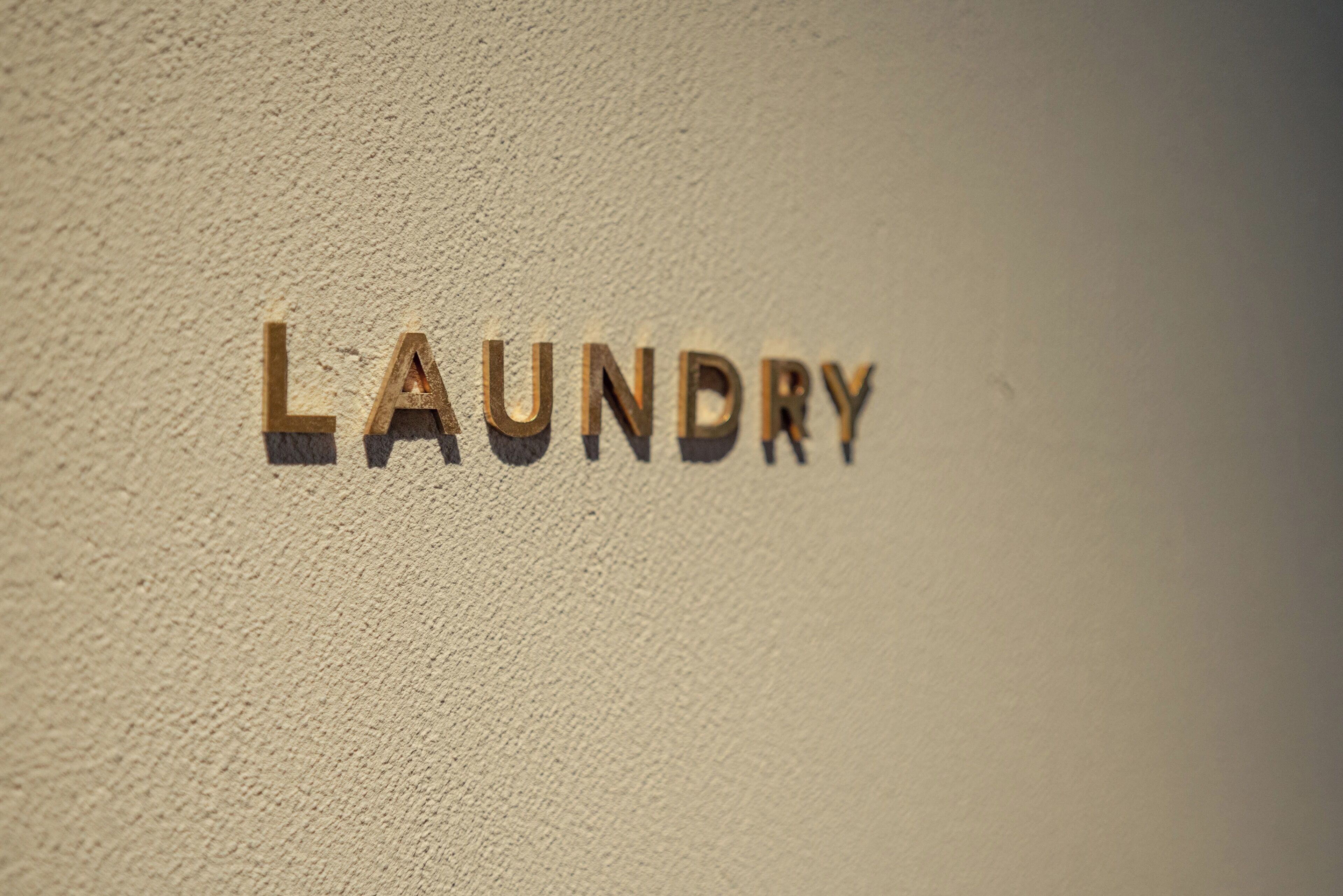 Das Wort "LAUNDRY" aus Holzlettern an einer strukturierten Wand.