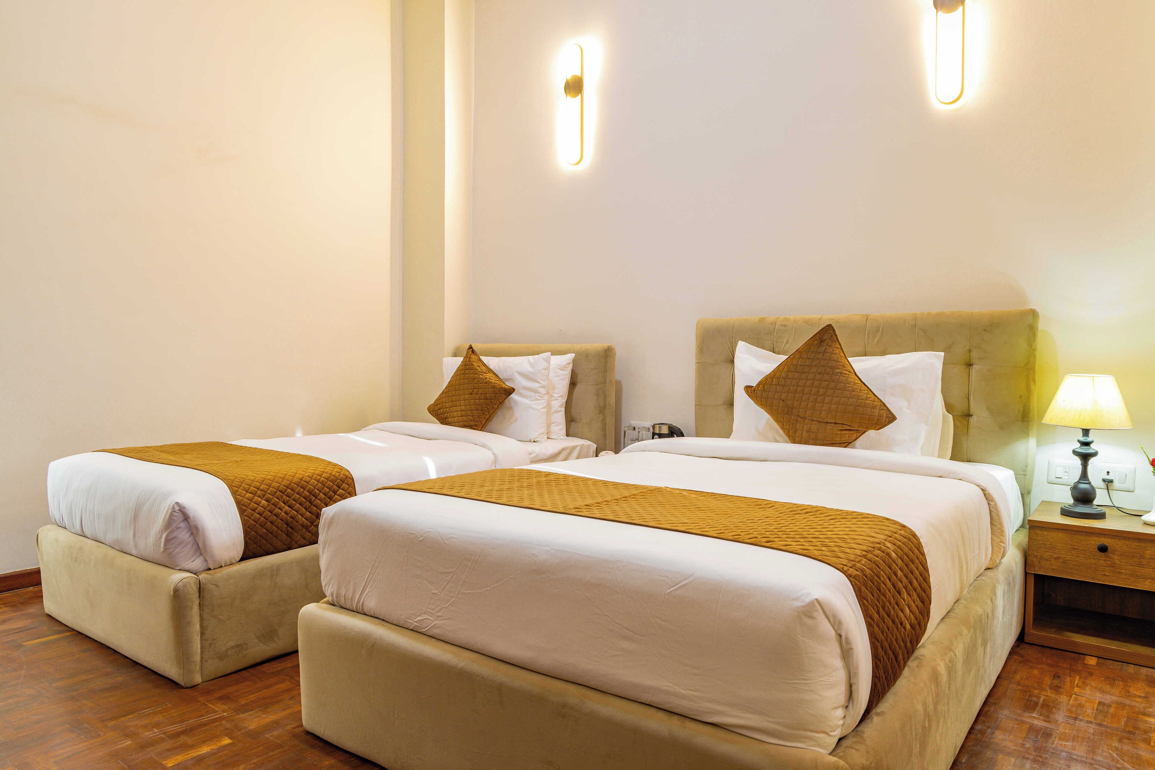 Habitación de hotel con dos camas, cada una con cabecera, mesita de noche con lámpara y suelo de madera.