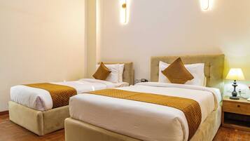 Habitación de hotel con dos camas, cada una con cabecera, mesita de noche con lámpara y suelo de madera.