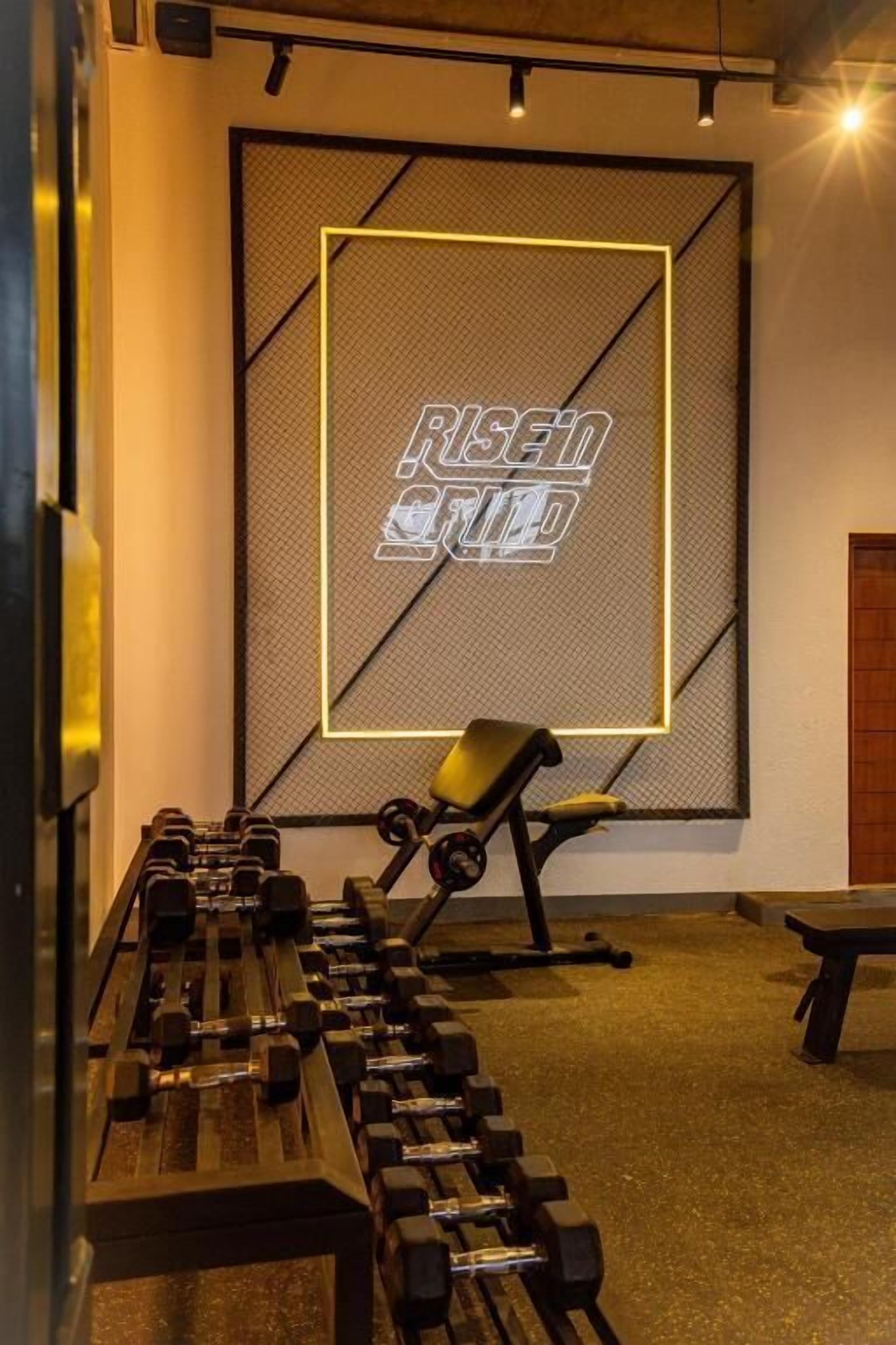 A gym with a bench, dumbbells, and a wall with 'RISE GRID' text.