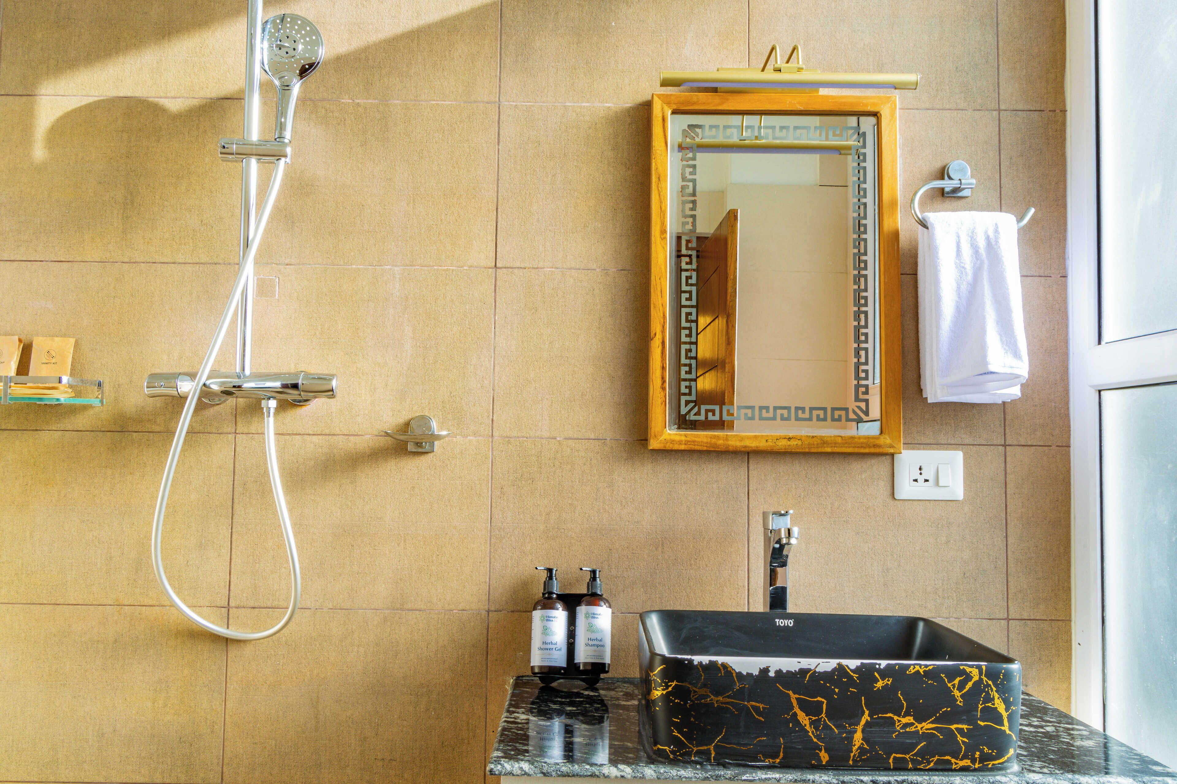 A bathroom with a shower, a sink with a black marble basin, a mirror with a decorative frame, and a towel rack with a white towel.