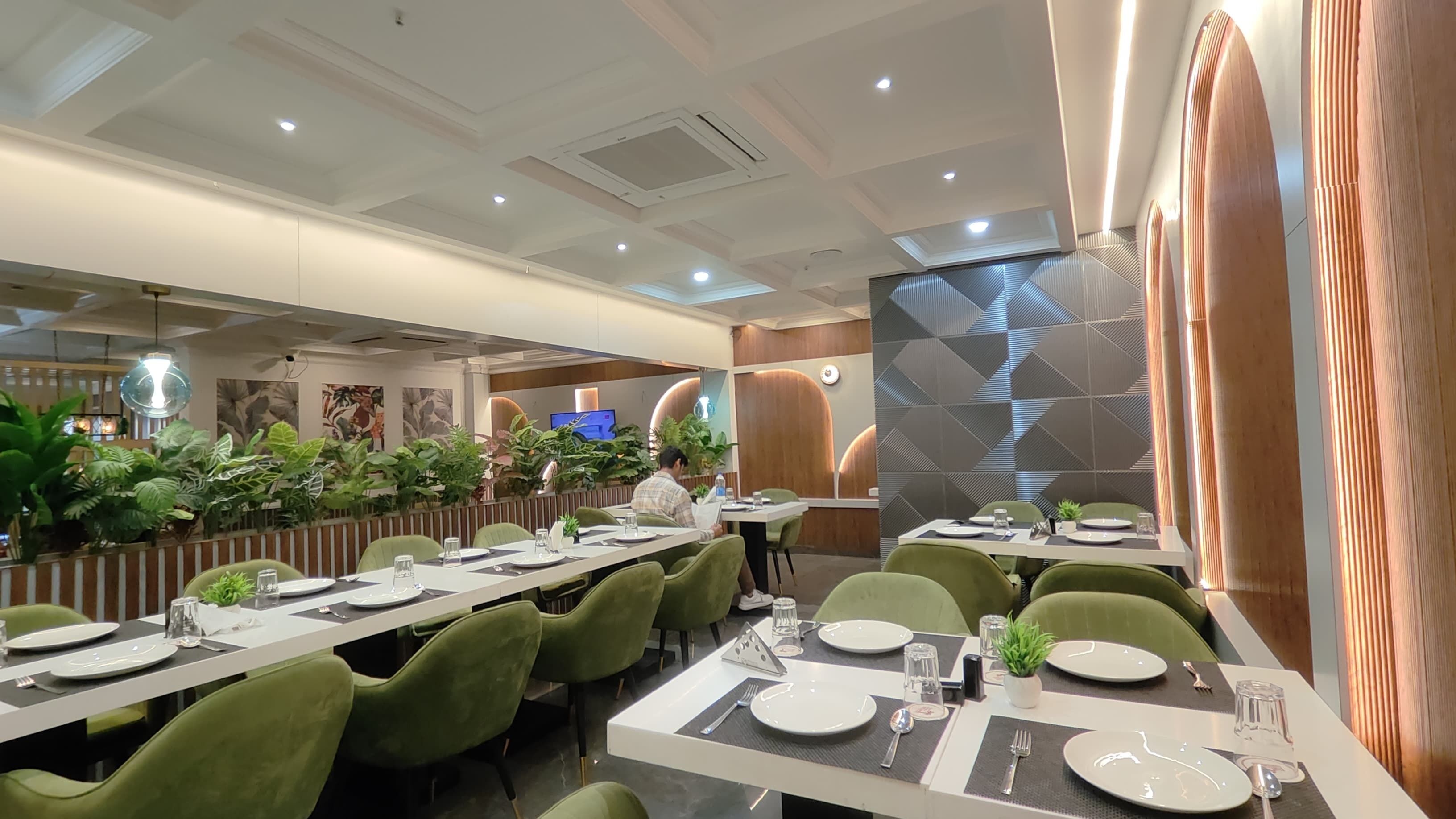 Un comedor moderno con mesas largas, sillas verdes y una variedad de plantas.