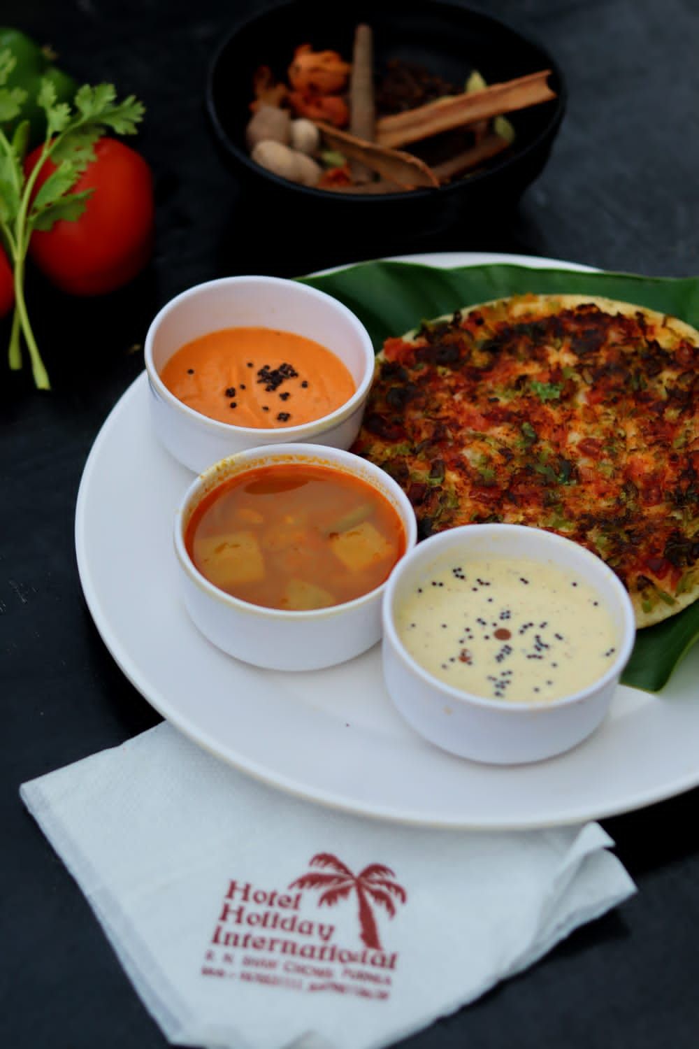 En tallerken med en grøntsagspandekage, to skåle med suppe og en skål med sauce, samt en tomat og en skål med nødder.