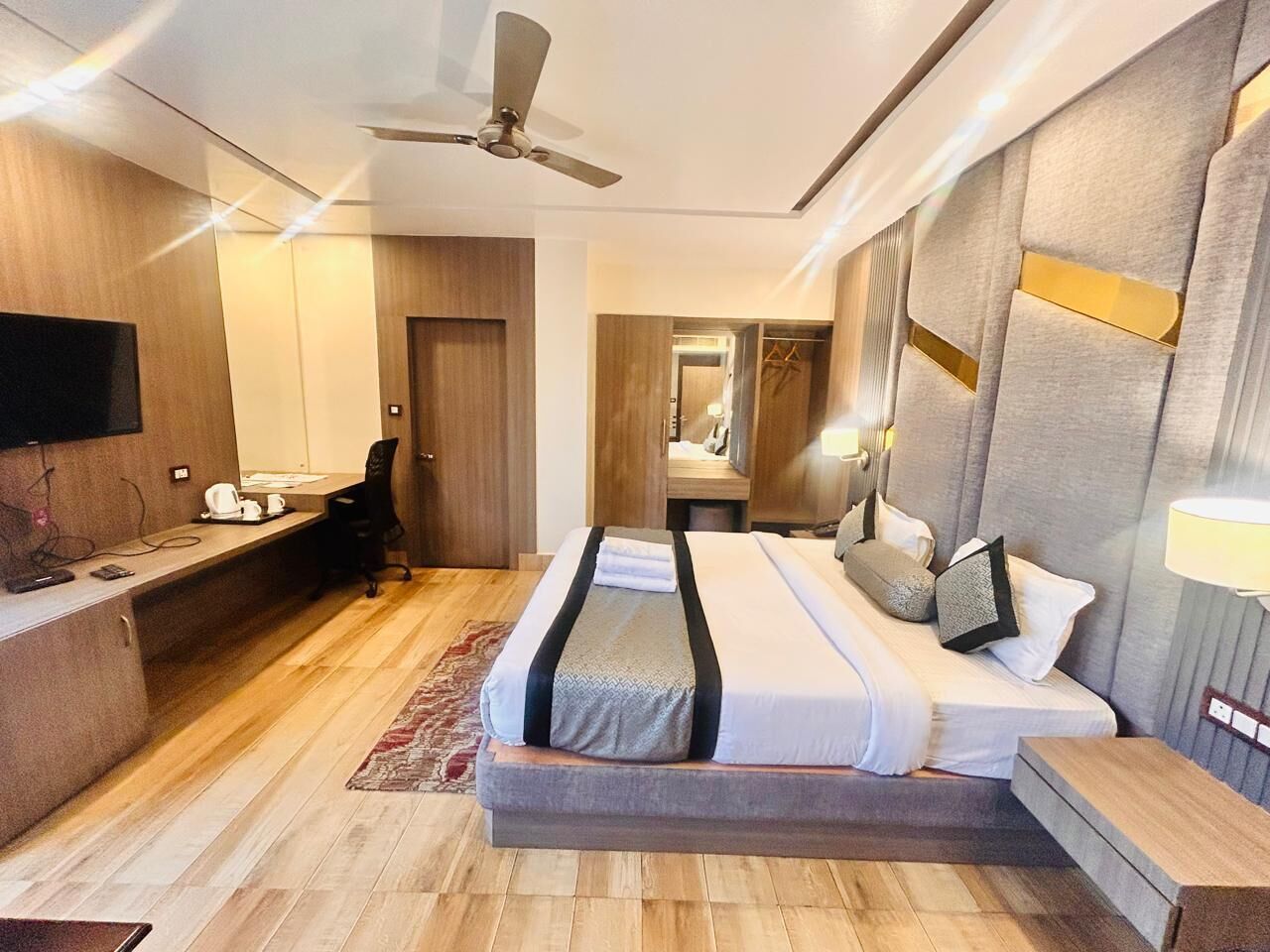 Een moderne hotelkamer met een groot bed, een bureau, een stoel, een televisie en een plafondventilator.
