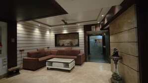 A modern living room with a sectional sofa, a coffee table, a decorative wall piece, and a ceiling fan. - Hotel Holiday international (Purnia)