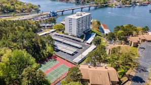 Un hotel de varios pisos con cancha de tenis, estacionamiento y vista al río.