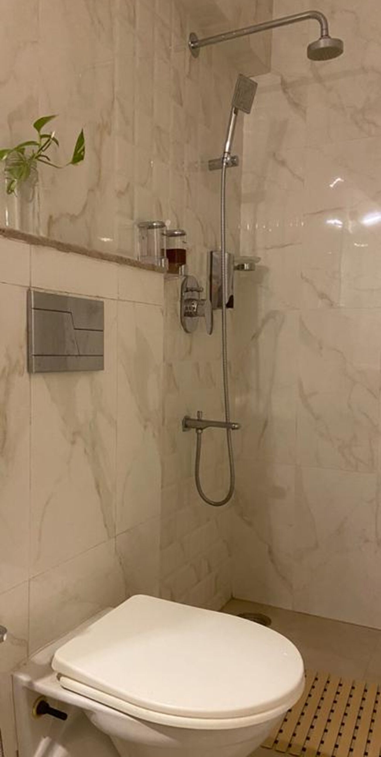Une salle de bain moderne équipée d’une douche, de toilettes et d’une petite étagère où sont rangés les articles de toilette.