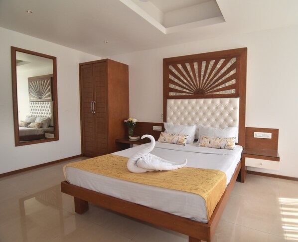A neatly arranged bedroom with a large bed, a wardrobe, a nightstand, and a mirror. - Beach Paradise Miramar Goa (Panaji)