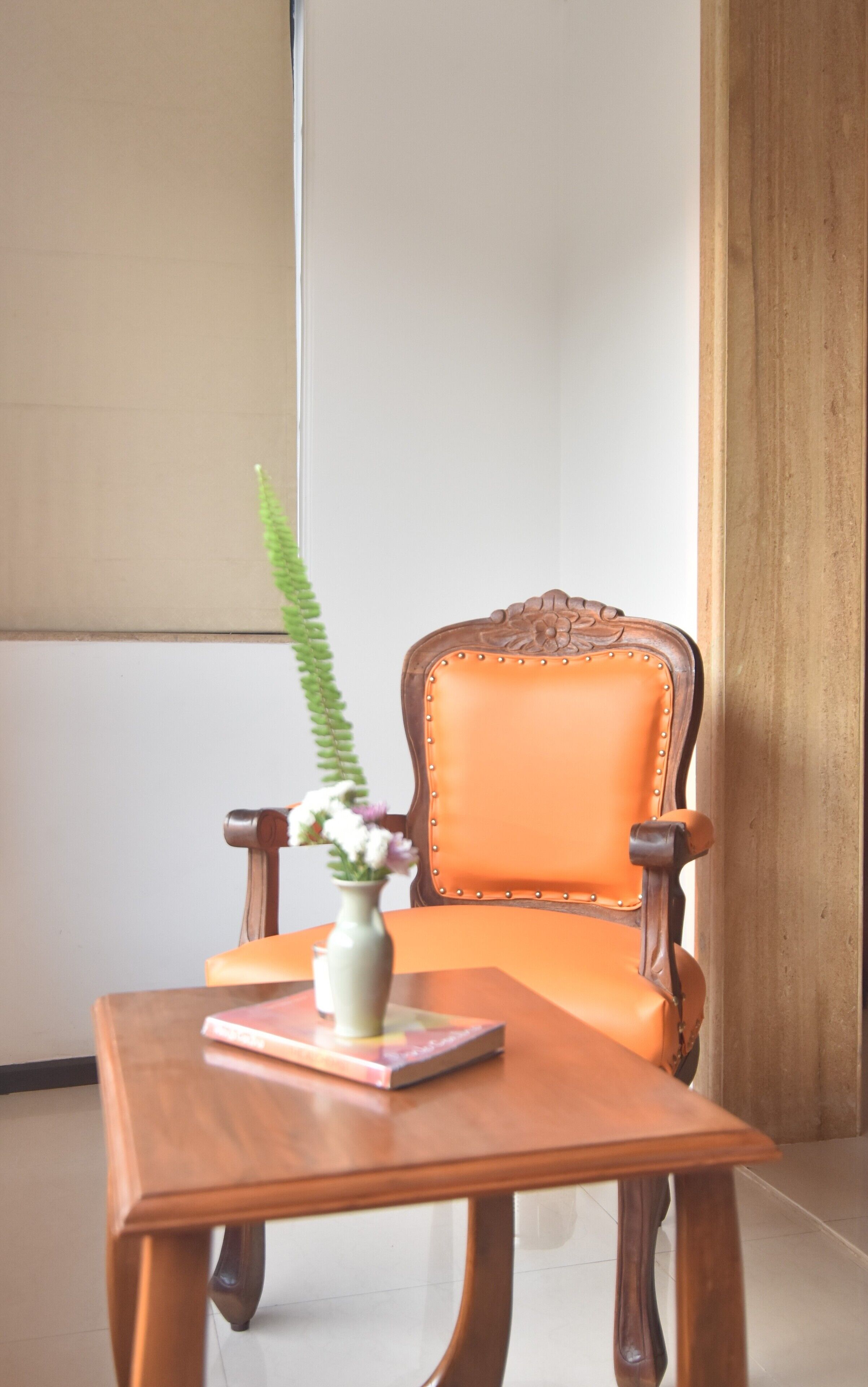 A wooden chair with a cushioned backrest and a small table with a vase and book.