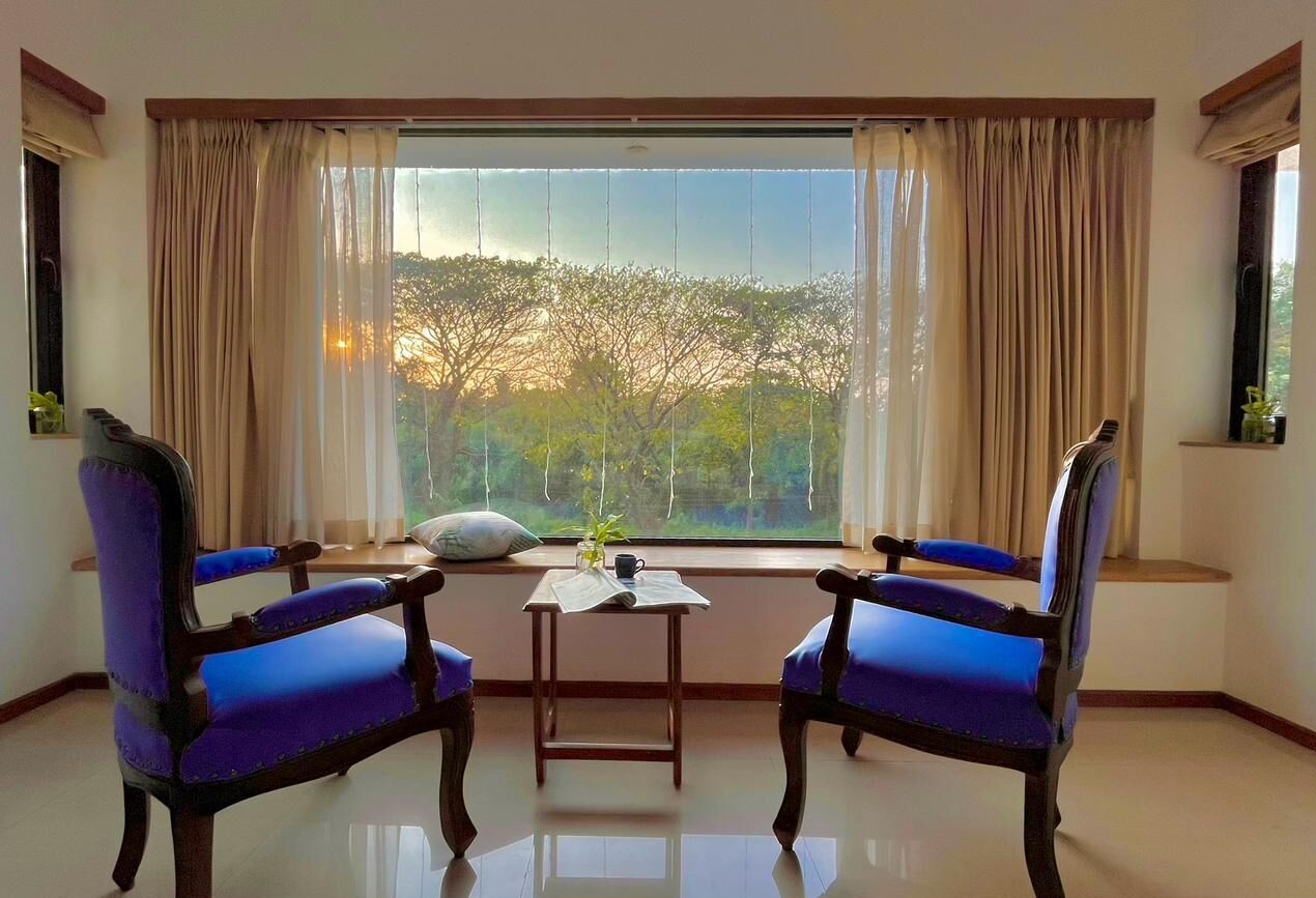 Una habitación con dos sillones tapizados en azul, una mesita con un periódico y una ventana con cortinas.