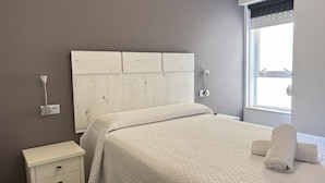 A bed with a white headboard, a bedside table with drawers, a window with blinds, and a wall socket. - Desconectaengalicia Ribapraia with Swimming Pool (Sanxenxo)