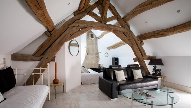 Ein modernes Loft mit freiliegenden Holzbalken, einem schwarzen Ledersofa, einem Glastisch und einer minimalistischen Einrichtung.
