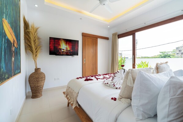 A modern bedroom with a large bed, a television mounted on the wall, and a view of greenery outside. - Salthouse Uluwatu (Pecatu)