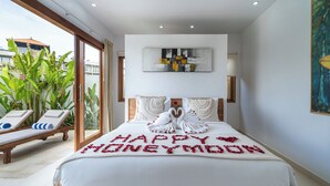 A spacious bedroom with a large bed, a balcony with lounge chairs, and a view of the outside. - Salthouse Uluwatu (Pecatu)