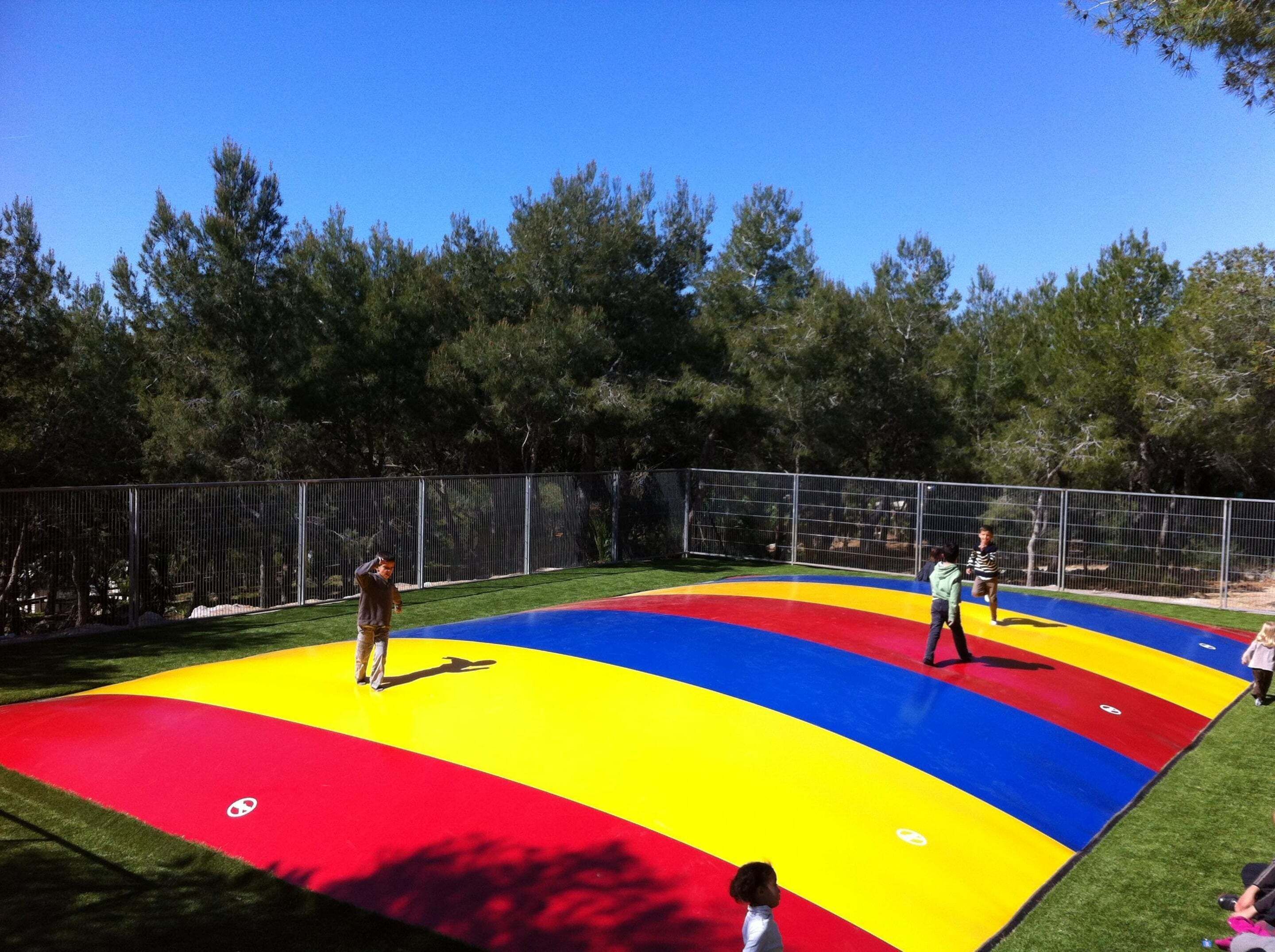 Zona de juegos al aire libre con superficie plana y colorida, rodeada por una valla.