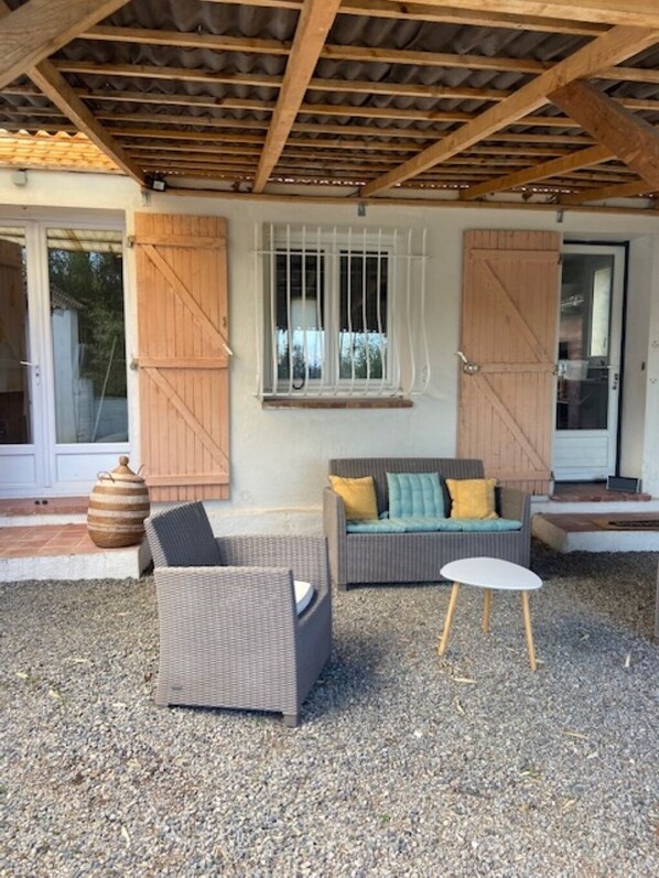 An outdoor seating area with wicker furniture, a small table, and a window with white bars.
