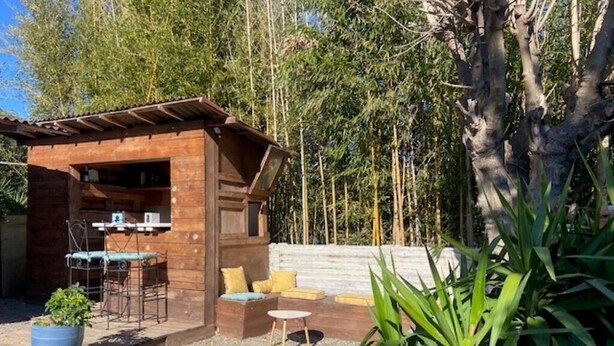 Une cabane en bois dot ée d’un patio comprenant une table et des chaises, le tout entouré de verdure.