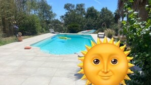 Une piscine sur laquelle est superposé un symbole d’un soleil, entourée de verdure et sous un ciel dégagé.